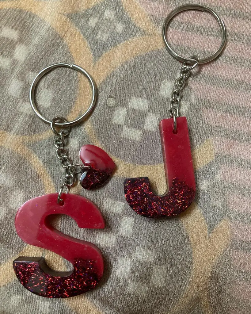 Red, sparkly resin letter 'S' keychains displayed on a textured fabric background.