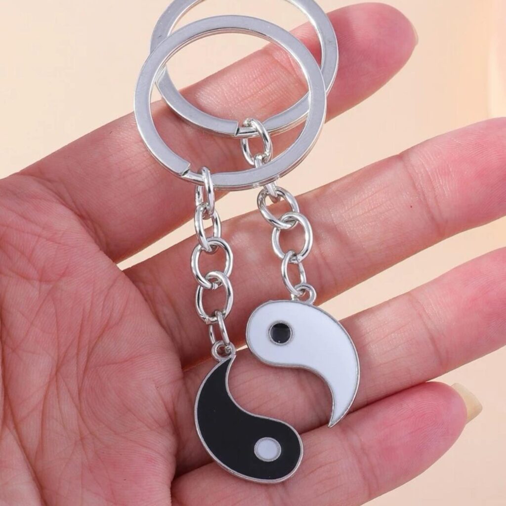 Yin yang symbol keychains in black and white, held in a hand, symbolizing balance.
