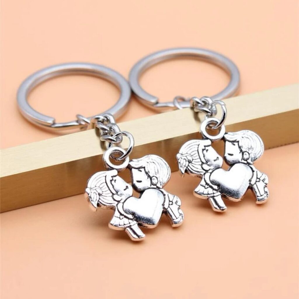 Two interlocking keychains depicting cartoon couples embracing, set against a soft peach background.