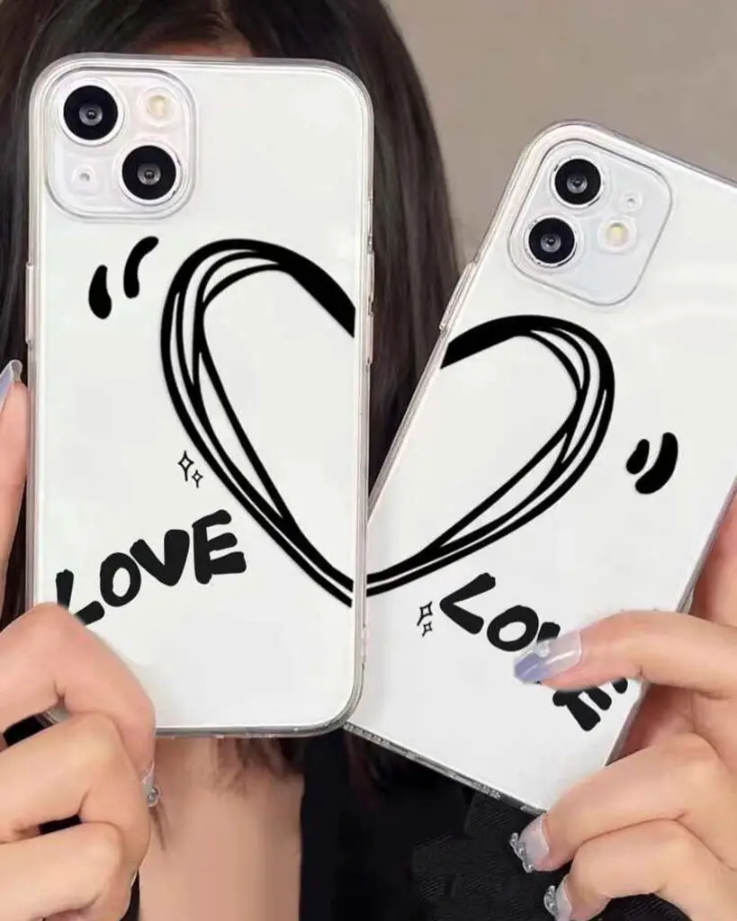 Two minimalist iPhone cases held up, displaying a large black heart and the word 'LOVE' in bold lettering, against a soft-focus background.