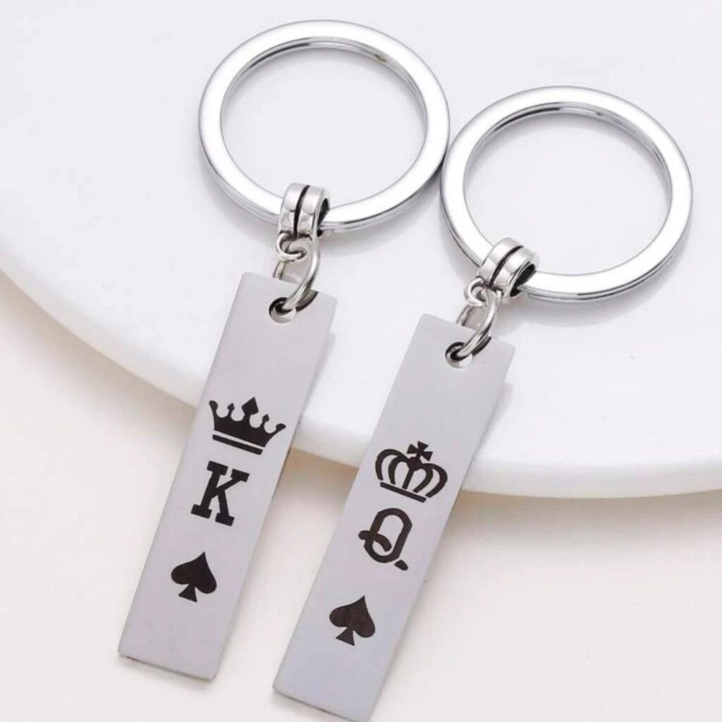 Silver keychains with black king and queen crown symbols, designed for couples, presented on a white circular plate.
