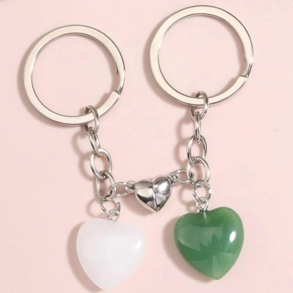 Two heart-shaped keychains, one white and one green, linked by a chain on a pink background.