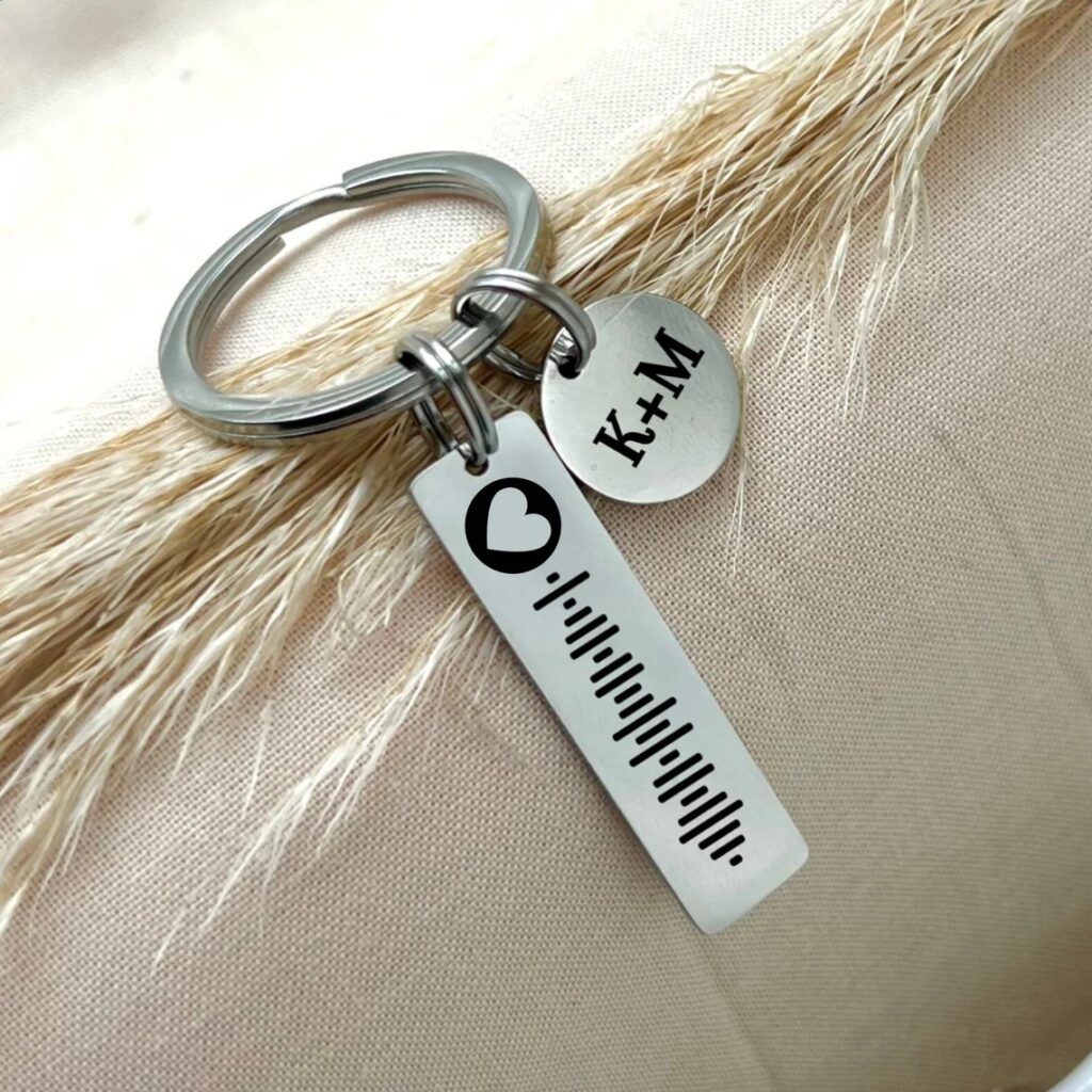 Silver keychain with a sound wave design and heart symbol, and a round pendant with the initials "K+M".