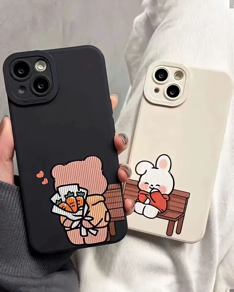 Two hands holding smartphones, each with a cartoon couple on a bench depicted on the cases, one with bears and one with a rabbit.