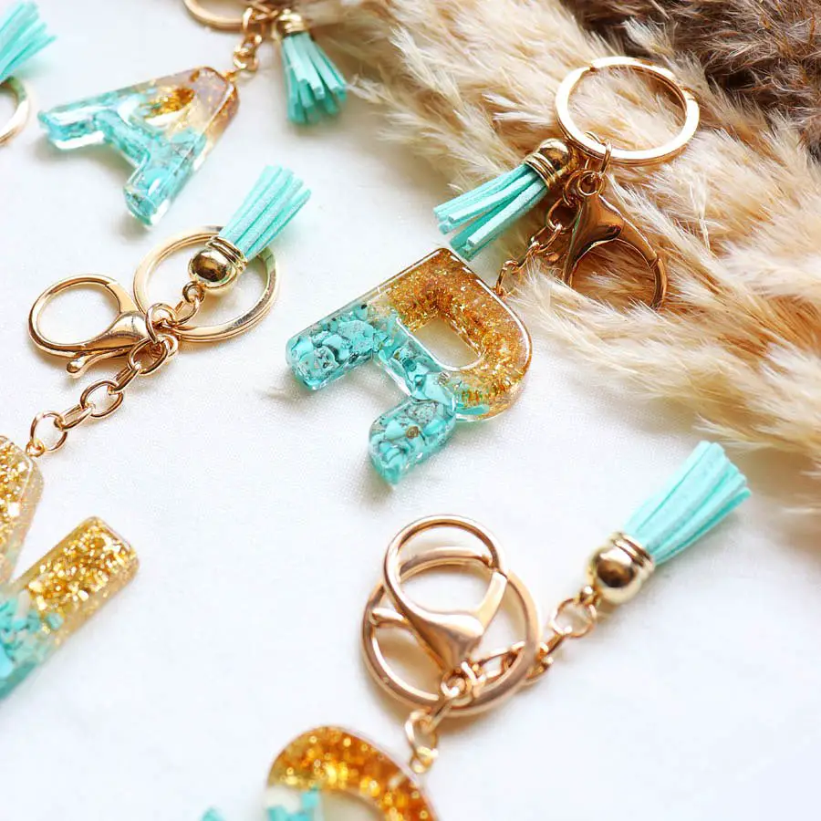 Colorful resin keychains shaped like letters with glitter, turquoise stones, and teal tassels.