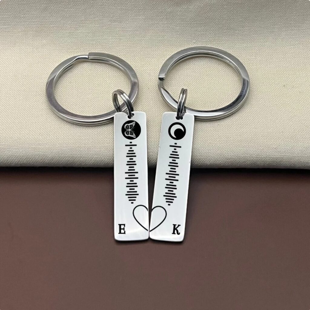 Two silver rectangular keychains with sound wave designs and initials, symbolizing a personal connection.