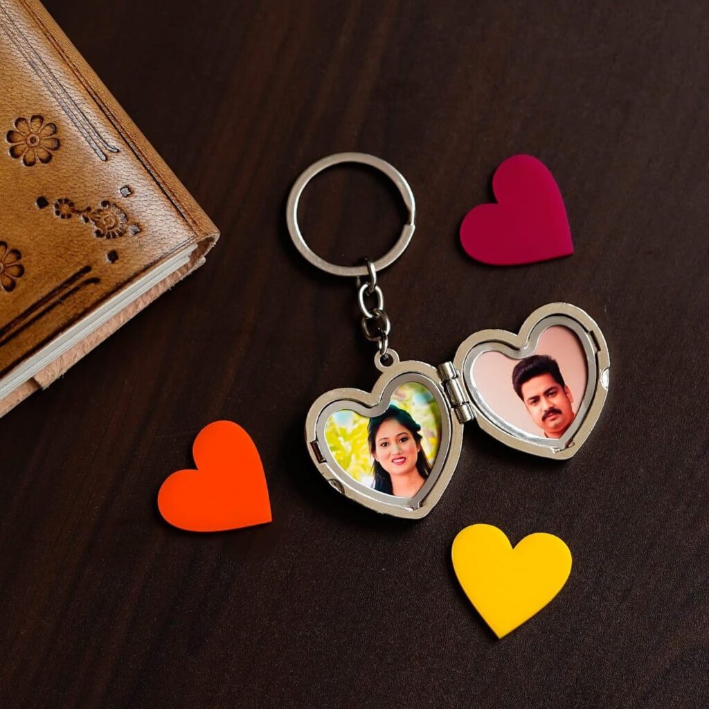 A heart-shaped keychain split into two, each half displaying a photo of a partner, with colorful hearts around on a wooden surface.