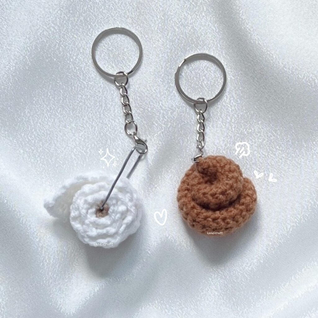 Two crochet keychains in the shape of poop emojis, one white and one brown, displayed on a silvery background.