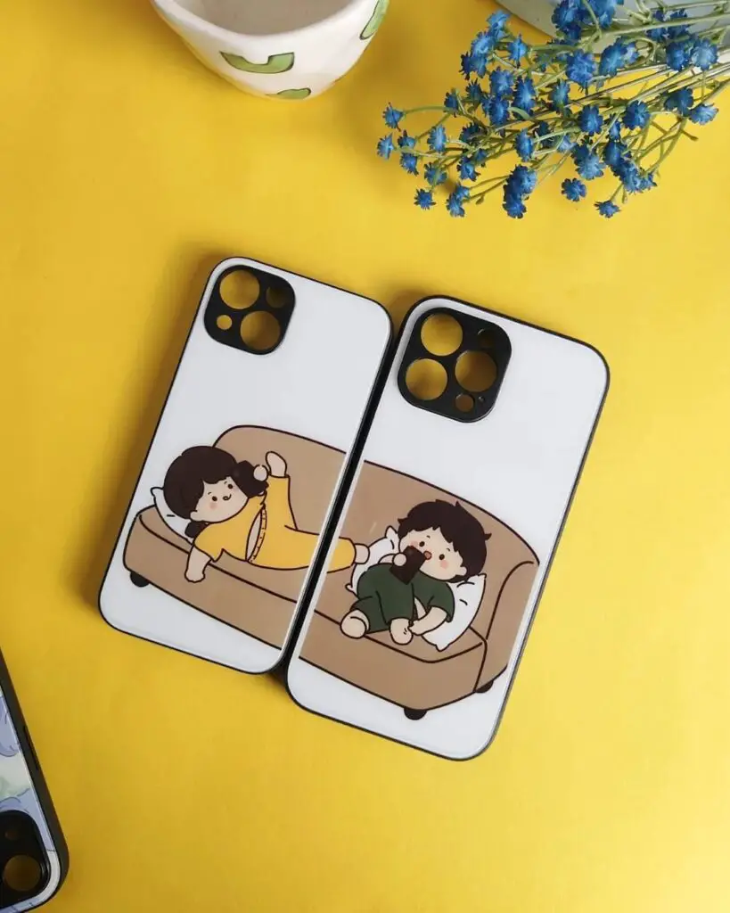Two iPhone cases with minimalist illustrations of characters lounging on sofas, one reading and one watching TV, set on a vibrant yellow background.