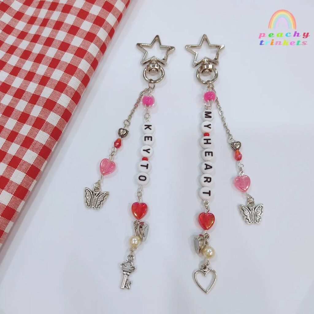 Two dangle keychains with charms and beads spelling out "Key to My Heart" on a checkered background.