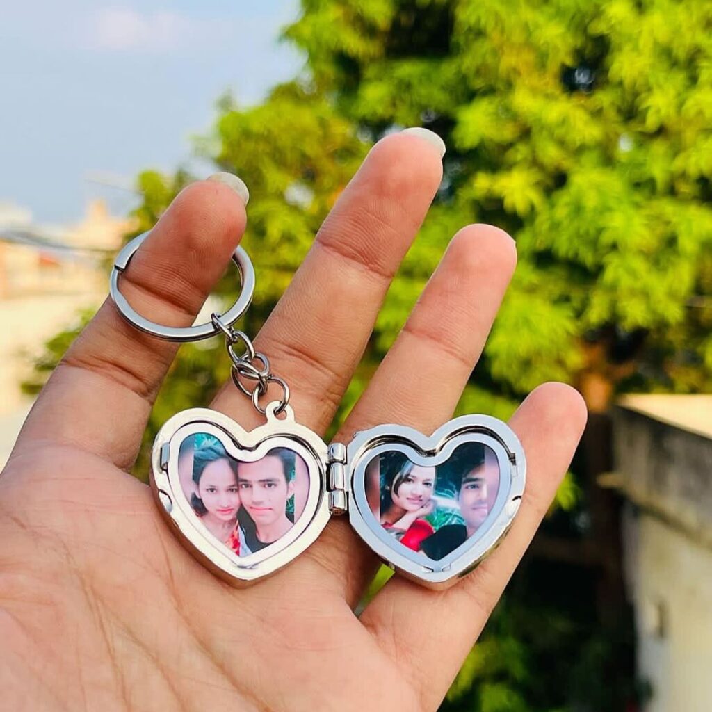A heart-shaped keychain displaying photos of a couple, held in hand with a green background.