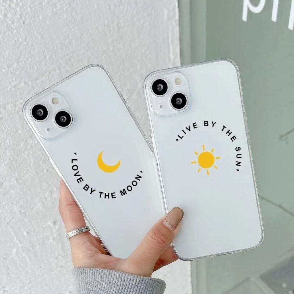 Two transparent iPhone cases with celestial designs; one with a moon and the phrase 'Love by the Moon' and the other with a sun and 'Live by the Sun'.