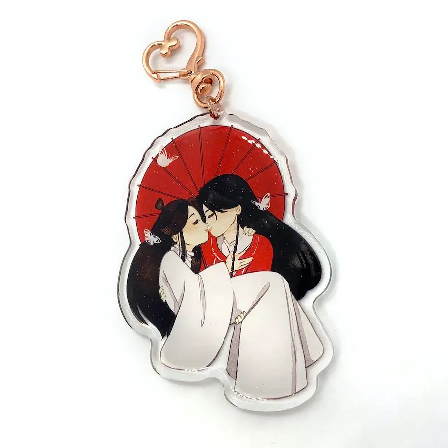 A keychain showing two anime characters kissing under a moonlit sky, surrounded by animal companions.