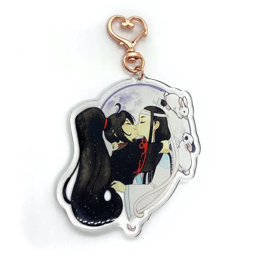 An illustrated keychain showing an anime couple kissing under a moonlit sky with animal companions, attached to a copper-colored clasp.
