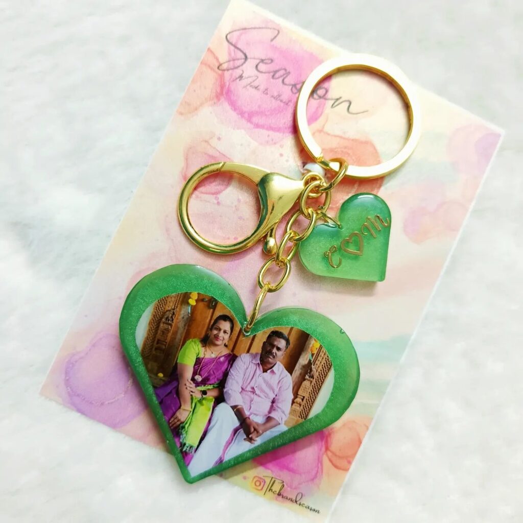 A green heart-shaped keychain displaying a couple's photo, with additional charms and the initials "CM".