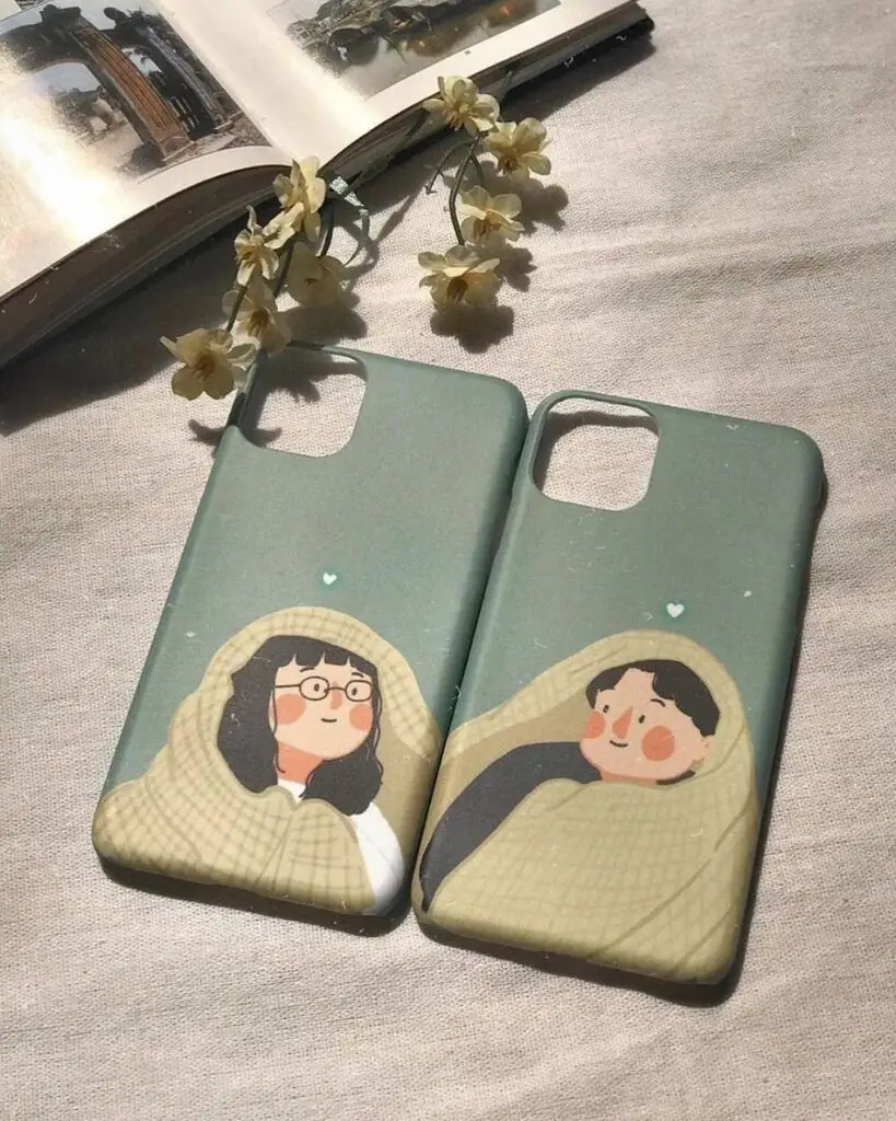 Two iPhone cases featuring illustrations of a couple wrapped in cozy blankets, depicted in soothing green tones, suggesting warmth and affection.