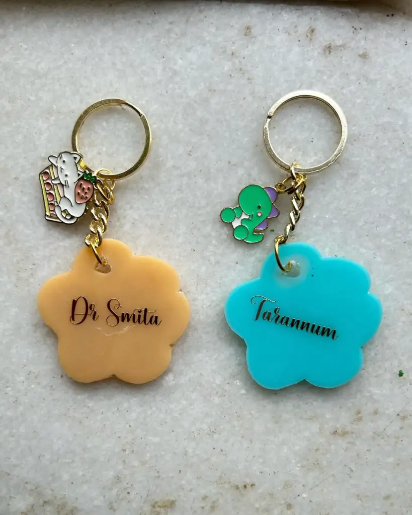 Two floral-shaped keychains with names, one in peach and one in sky blue, ideal for personalization and gifts.