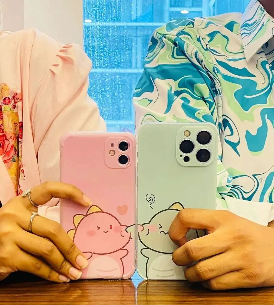 Two people holding iPhone cases with cute animal designs, one pink with a cat and one green with an elephant, in a vibrant restaurant setting.