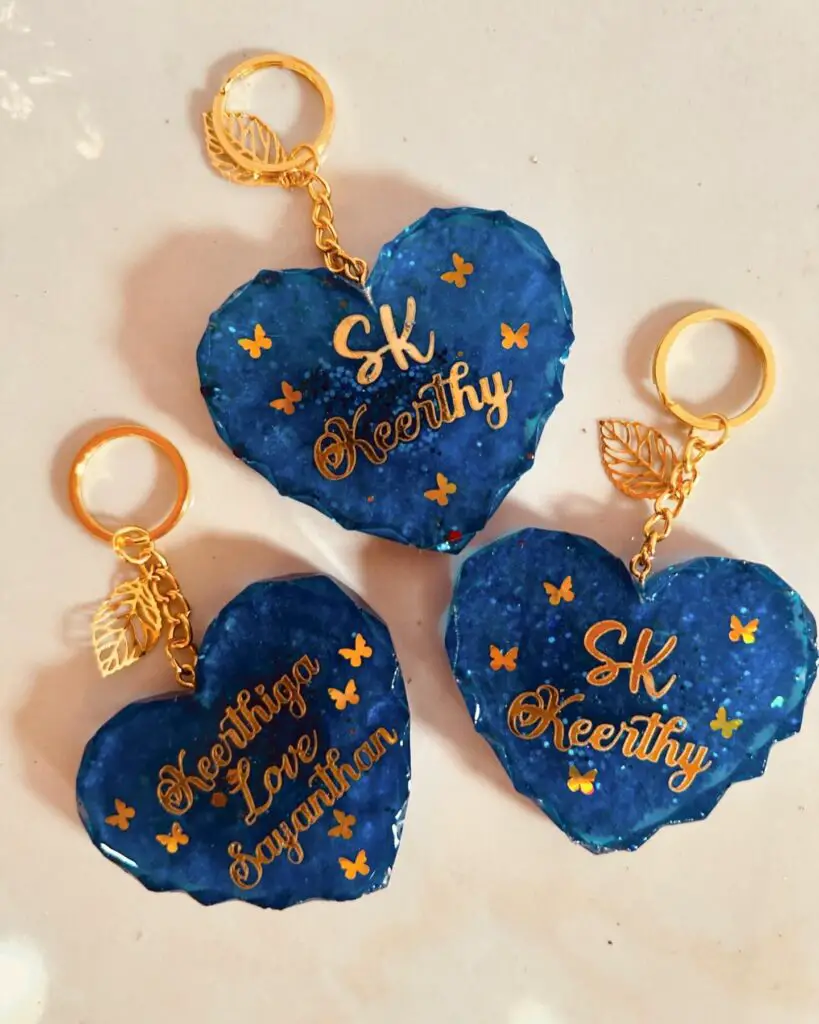 Three custom heart-shaped keychains in deep blue with gold lettering and small decorative elements.