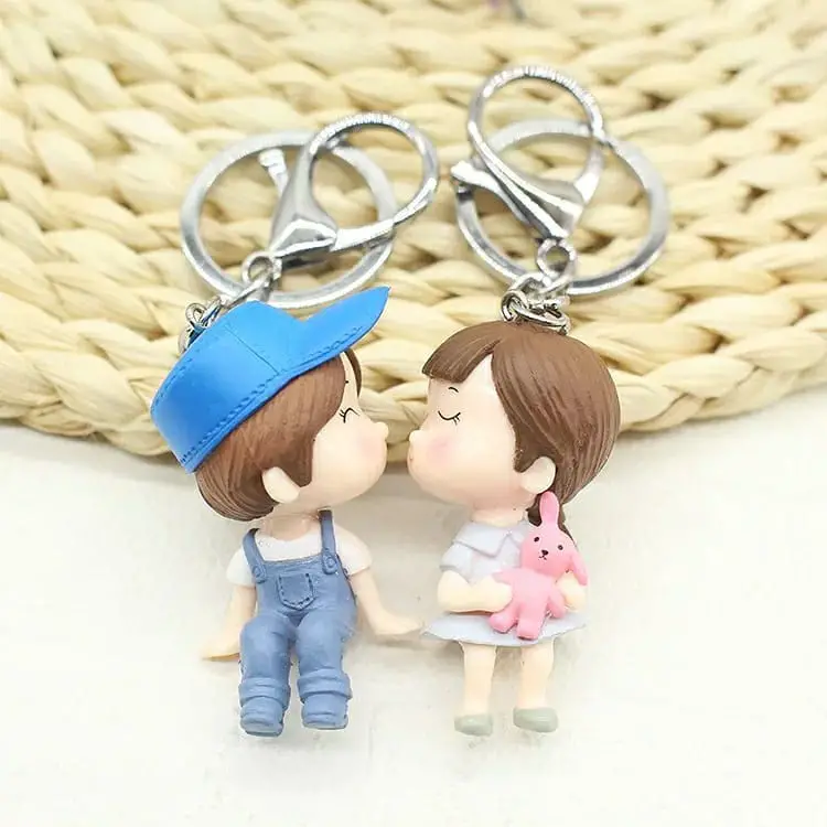 Two cartoon-style keychains depicting a boy and a girl in a kissing pose, the boy in blue and the girl in pink.