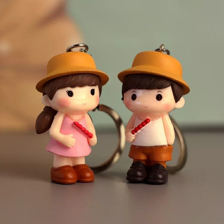 Cartoon keychains of a young couple, each holding a red flute and wearing a yellow hat, showcased in a casual setting.