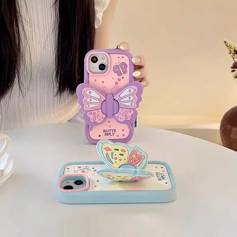 Two iPhone cases with butterfly designs, one with a large purple butterfly and the other with a collection of smaller butterflies and flowers, displayed in a whimsical setting.