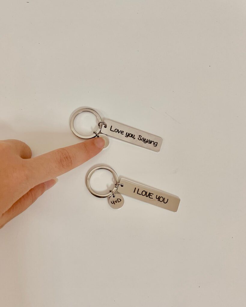 Two minimalist keychains with romantic messages, "I Love you, Sayang" and "I LOVE YOU", on a plain background.