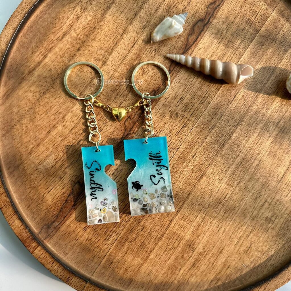 Two puzzle piece keychains with names and beach-themed designs, featuring sand and shells on a wooden backdrop.