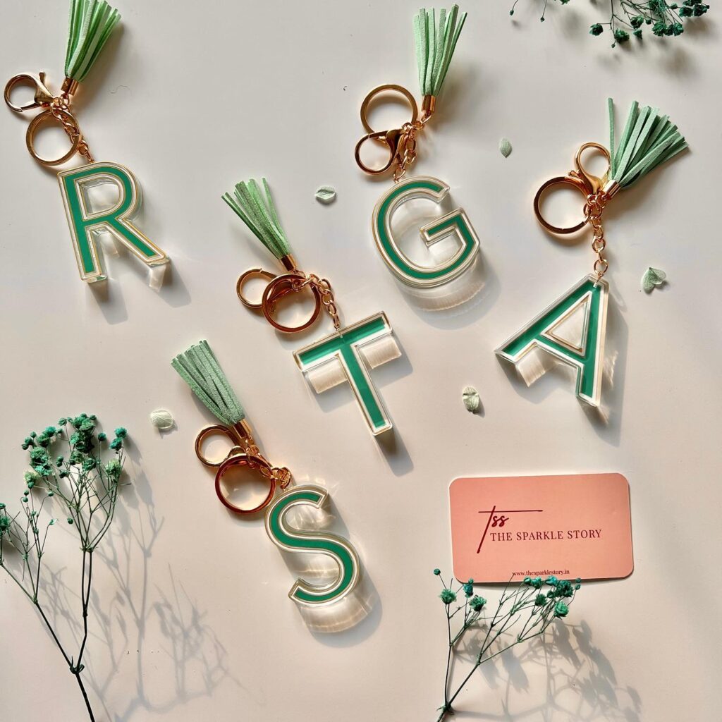 Stylish monogram keychains with green and white stripes and green tassels, arranged artistically.