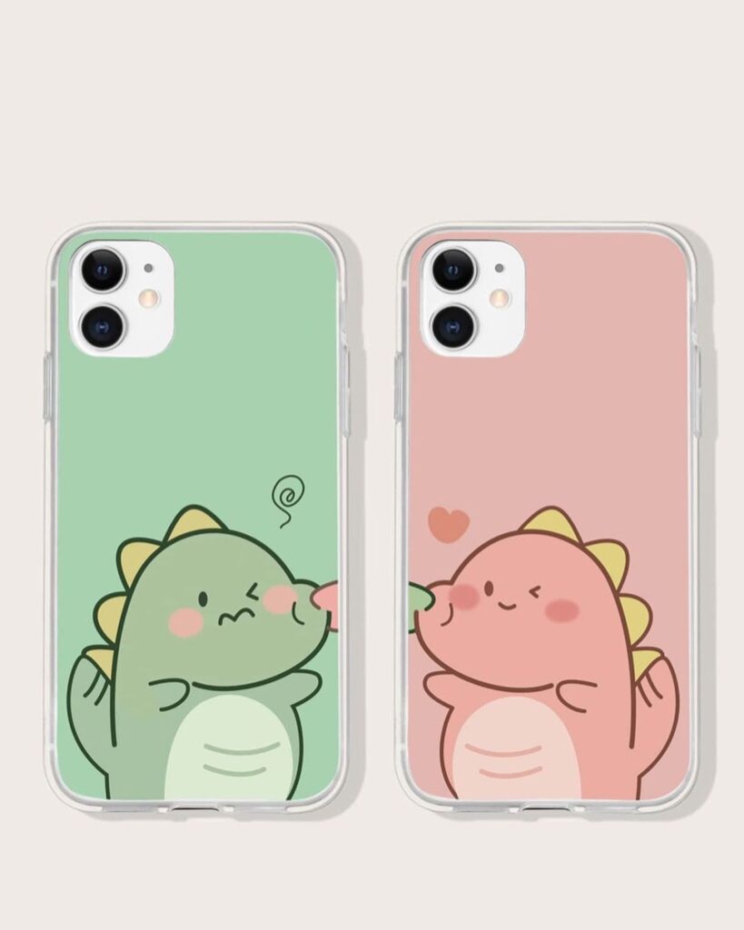 Two smartphones with cases featuring a green and pink cartoon dinosaur couple kissing, set against matching color backgrounds.