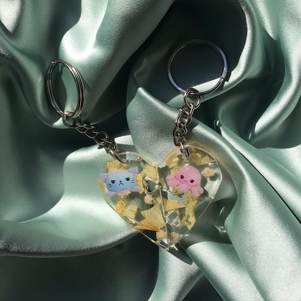 Two-part heart-shaped keychain featuring cartoon characters, a blue cat, and a pink octopus on a silky background.