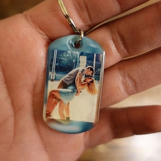 Personalized photo keychain depicting a couple kissing, held in hand against a blurred background.